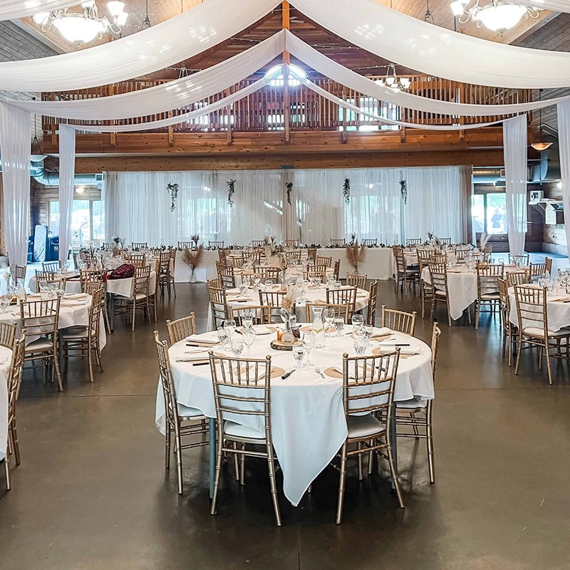 Chic wedding reception with white drapes, rustic chairs, and beautiful table settings for a once-in-a-lifetime celebration.