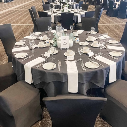 Beautifully arranged round table with black and white linens, fine dinnerware, and floral centerpiece for special events.